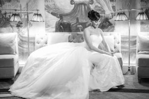 A bride in an elegant white ball gown sits gracefully on a luxurious couch in a classic black and white photograph.