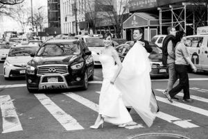 A person in a flowing white wedding dress crosses a busy city street in black and white photography.