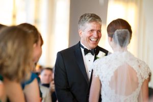 A joyful moment captured during a formal wedding ceremony as the groom smiles brightly in his black tuxedo.