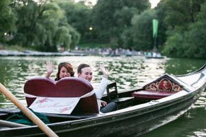 Couple enjoying a romantic gondola ride on a lake surrounded by lush greenery in Central Park.