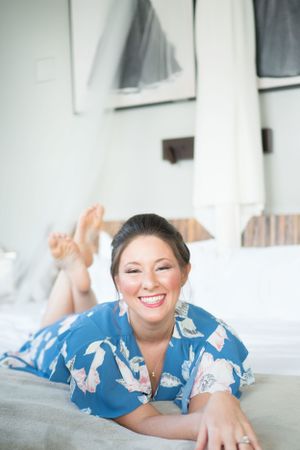 Person wearing blue and white floral print pajamas relaxes on white bedding while smiling at camera.