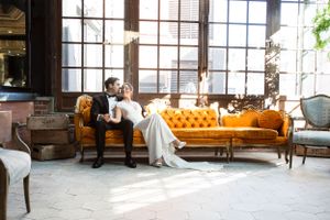 Elegant vintage-style seating arrangement with bright orange tufted sofa and antique furniture in a sunlit industrial space.