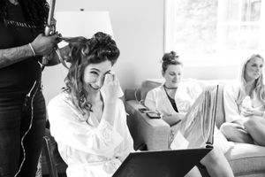 Black and white image of a hair styling session in progress with people gathered in a bridal preparation setting.
