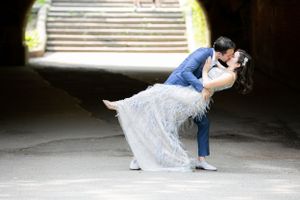 A couple shares a romantic dip kiss in a tunnel with stone stairs visible in the background.