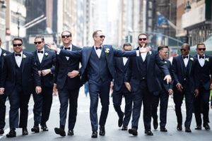 A group of groomsmen wearing black and navy suits walking confidently down a city street.