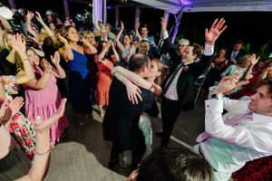 A crowded dance floor at a wedding reception with guests dancing energetically under purple lighting.