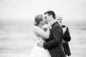 A romantic black and white beach wedding scene shows a couple sharing a kiss while officiant stands in background.