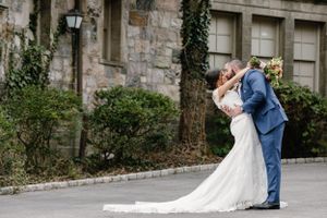 A romantic wedding couple shares a tender moment outside a rustic stone building with ivy-covered walls.