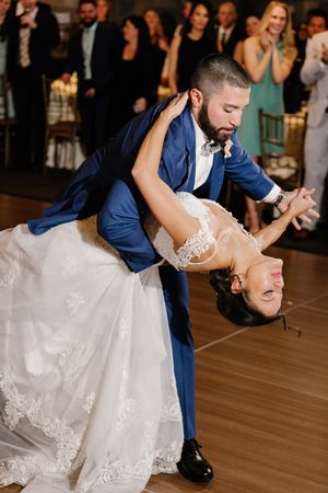 A couple performs a romantic dip during their first dance at a wedding reception while guests watch in the background.