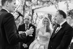 A black and white photograph of a wedding ceremony under a floral arch during an outdoor celebration.
