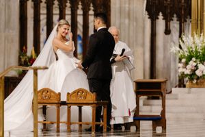 A traditional wedding ceremony takes place inside a grand cathedral with ornate gothic architecture and floral decorations.