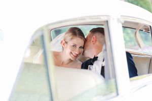 A bride and groom share an intimate moment in the back seat of a classic car on their wedding day.
