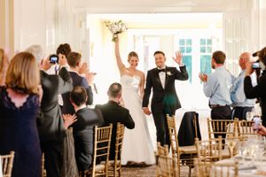 A joyful celebration with guests standing and clapping during a wedding reception in an elegant white ballroom.