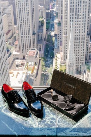 Dress shoes and accessories displayed on a glass ledge overlooking New York City skyscrapers from a high vantage point.