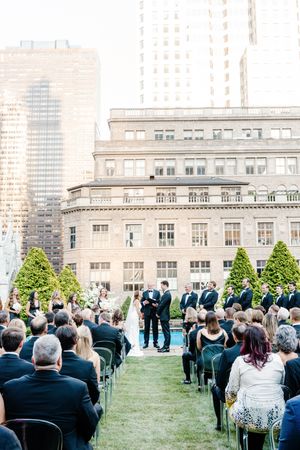 An outdoor wedding ceremony on a grassy rooftop with historic city buildings in the background.