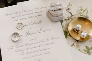 Wedding invitation with gold rings, pearls and white flowers on a delicate light background.