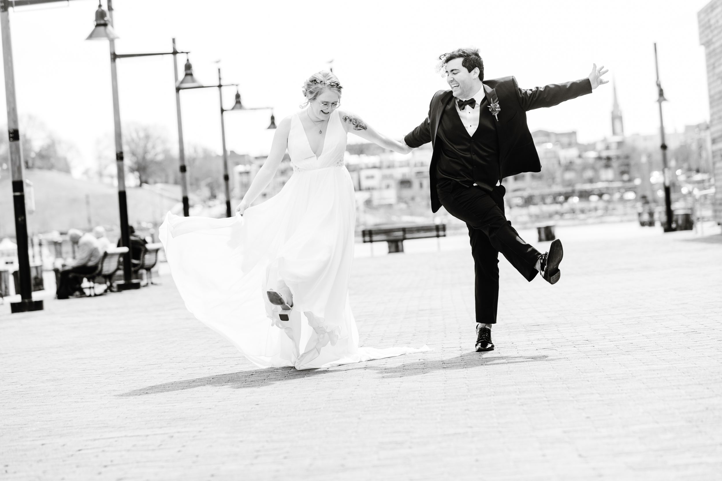 A joyful bride and groom dance playfully together on a city street, captured in elegant black and white photography.