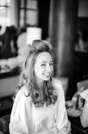 A joyful woman in a white top laughs while getting ready, captured in black and white photography.