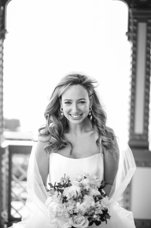 Black and white portrait of a bride in a white dress holding a floral bouquet and smiling on her wedding day.