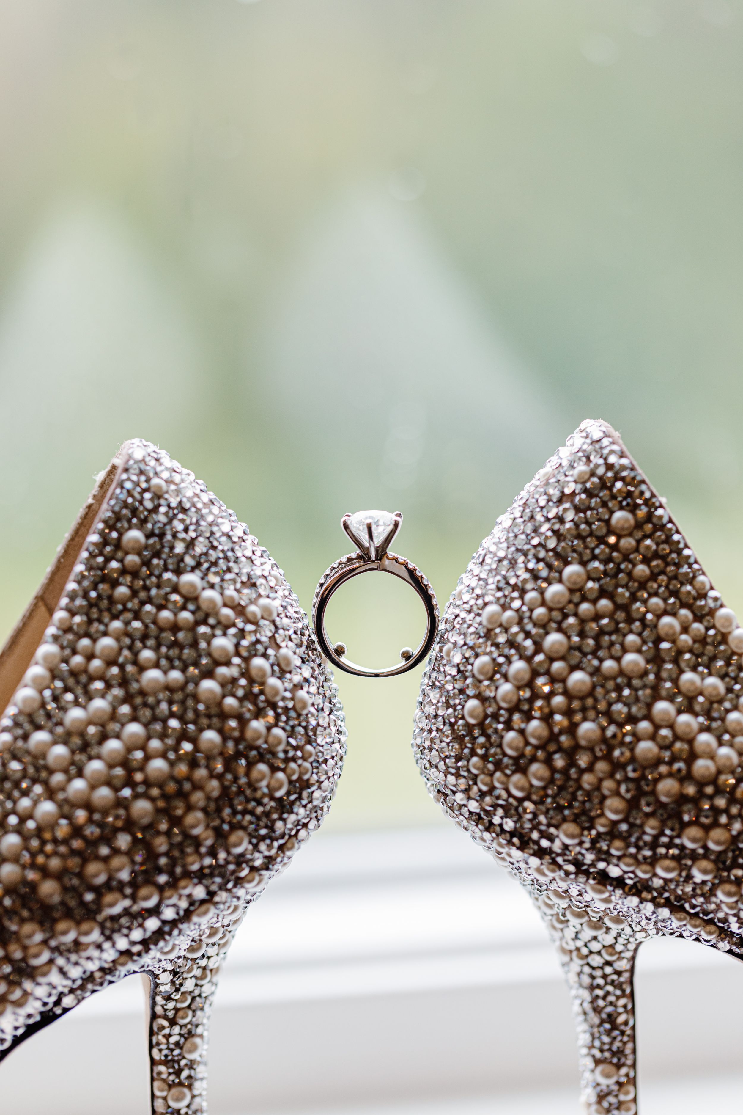 Diamond engagement ring artfully positioned between two glittering crystal-encrusted high heel shoes.