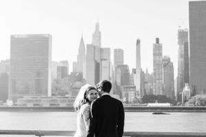 A couple gazes at the New York City skyline across the water in black and white.