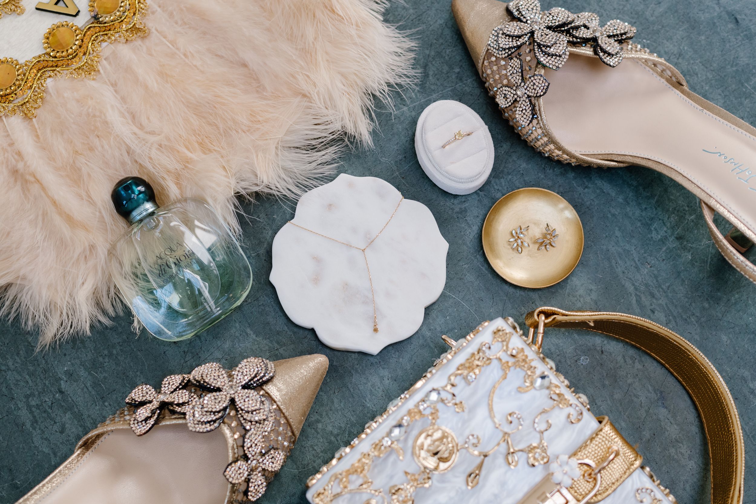 Luxury fashion accessories including snake print shoes, perfume bottle, and white cosmetic products on dark background.