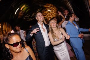 Party guests dancing and celebrating at a nighttime event with blurred lighting effects in the background.
