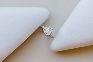 An elegant emerald cut diamond engagement ring nestled between white silk fabrics.