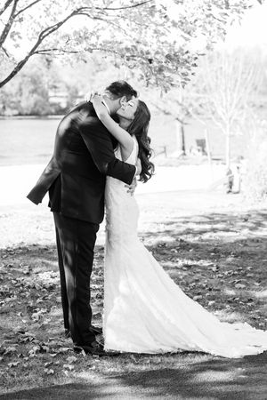 A romantic black and white wedding photo showing a couple embracing outdoors under blooming trees.