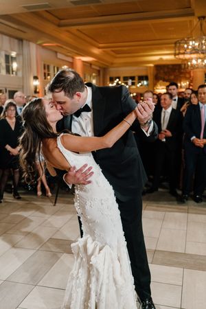 Couple shares romantic first dance at elegant ballroom wedding reception with guests watching and chandeliers overhead.