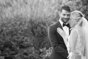 A romantic black and white wedding portrait of a bride and groom sharing an intimate moment outdoors.
