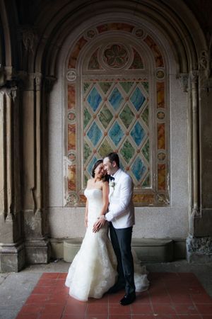 A couple shares an intimate moment under an ornate archway with decorative stained glass and architectural details.