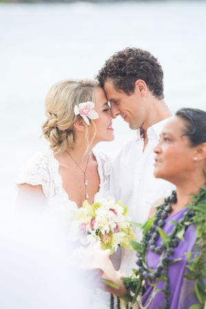 Romantic wedding ceremony on a beach with white and yellow flowers and purple leis in Hawaii.
