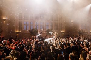 A crowded concert venue filled with enthusiastic fans while a performer crowd surfs above the audience in atmospheric lighting.