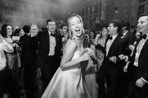 A joyful wedding celebration scene captures a bride in white dress laughing surrounded by guests at a formal reception.