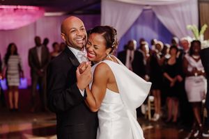 A joyful couple shares a first dance at their wedding reception, bride in white gown, groom in black tuxedo.