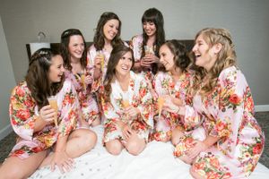 A group wearing matching floral robes sits together on a white bed laughing and enjoying a celebratory moment.