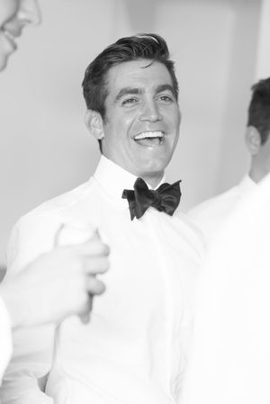 A cheerful person in a crisp white tuxedo jacket and black bow tie laughs while looking to the side.