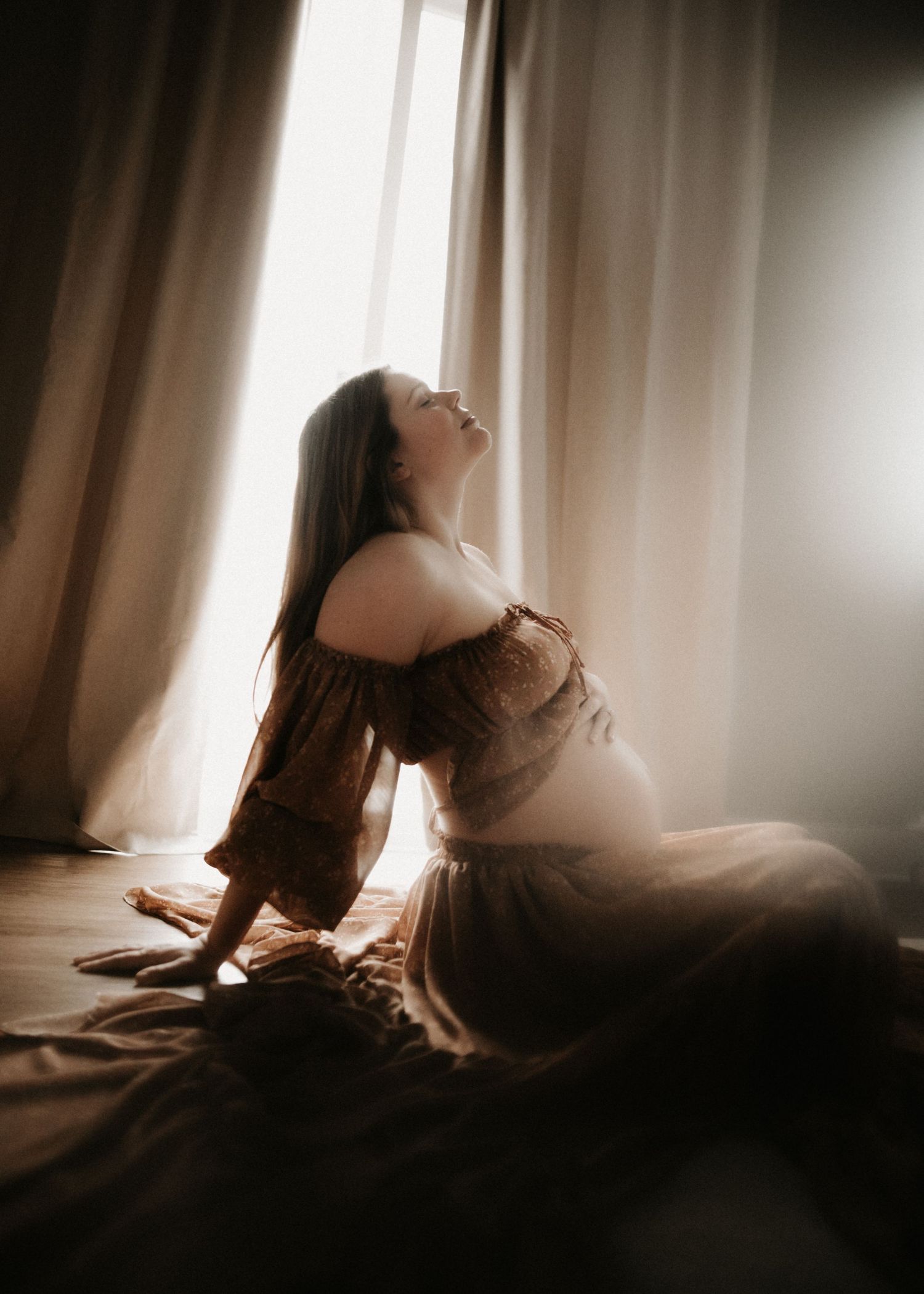 Artistic silhouette of woman in flowing dress sitting by window with dramatic lighting.