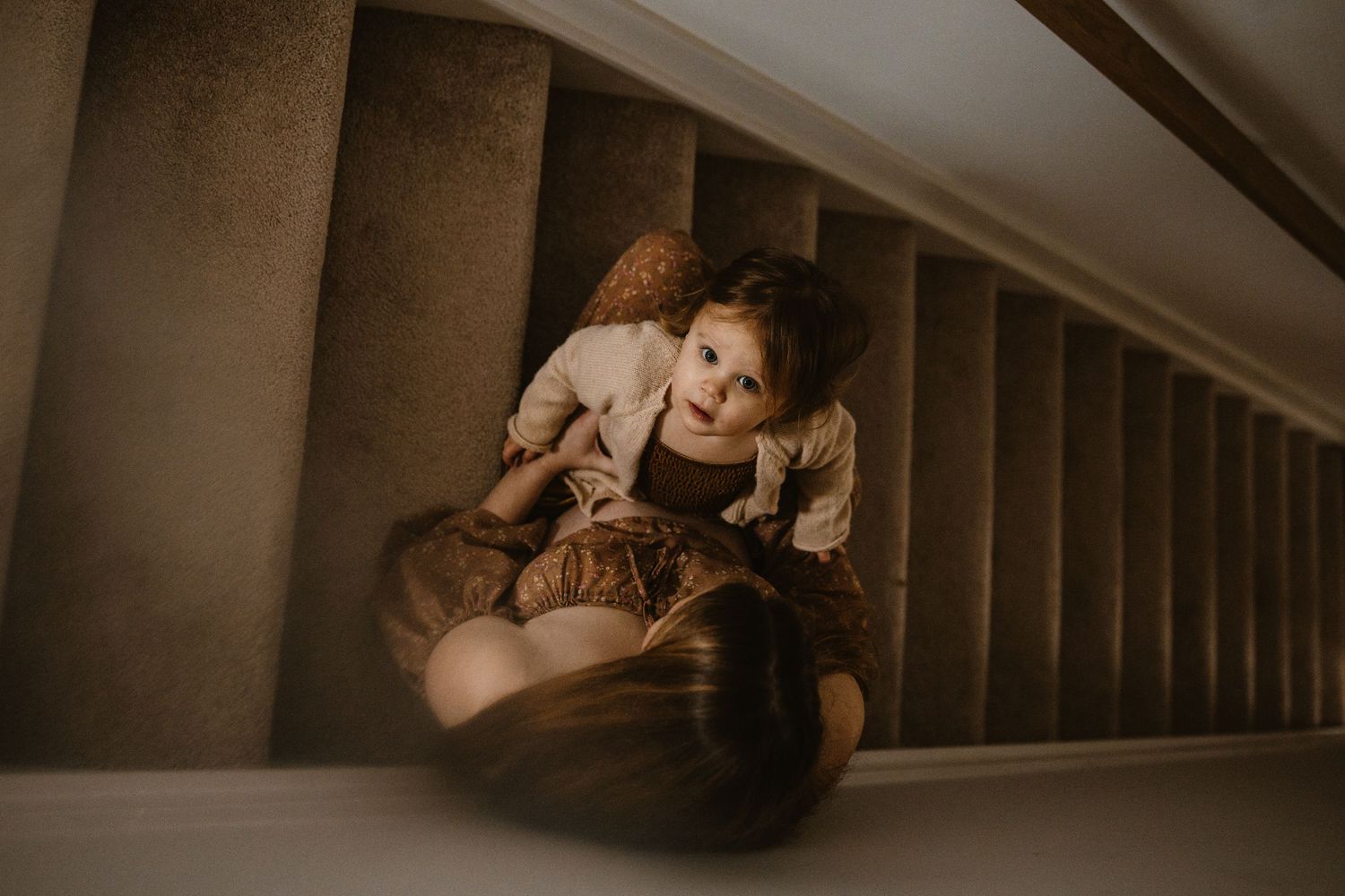 A woman in a black dress poses seductively on a wooden floor in a dimly lit attic space.