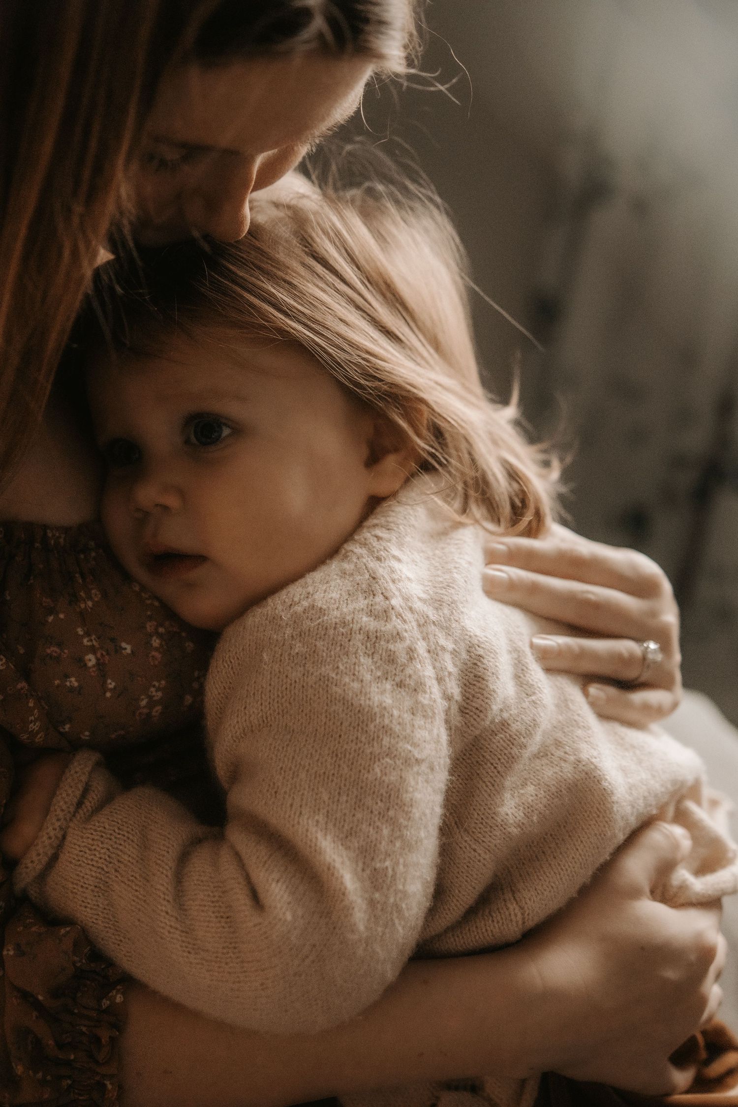 Intimate moody portrait of parent and child embracing in soft natural light wearing neutral tones.