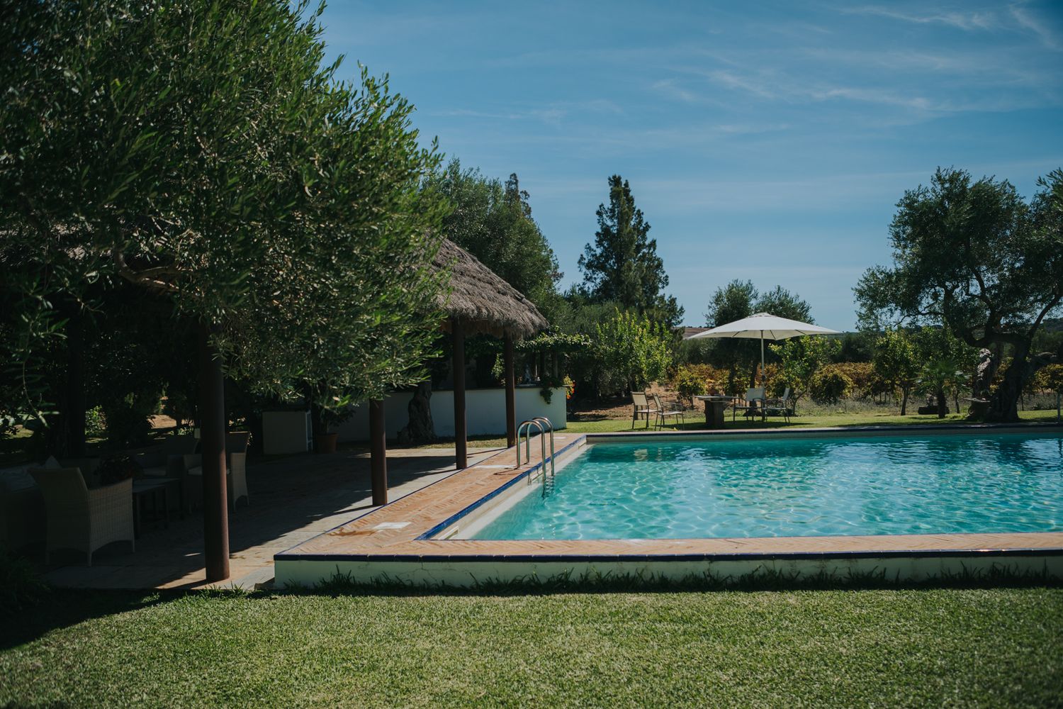 Luxurious outdoor swimming pool with covered cabana and landscaped lawn on a sunny day.