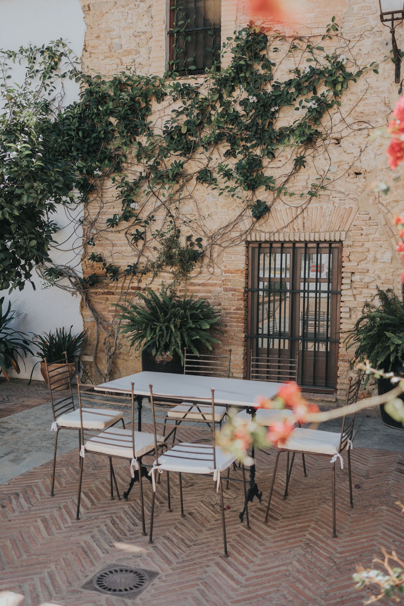 A charming courtyard seating area with metal chairs and climbing vines against a stone wall.