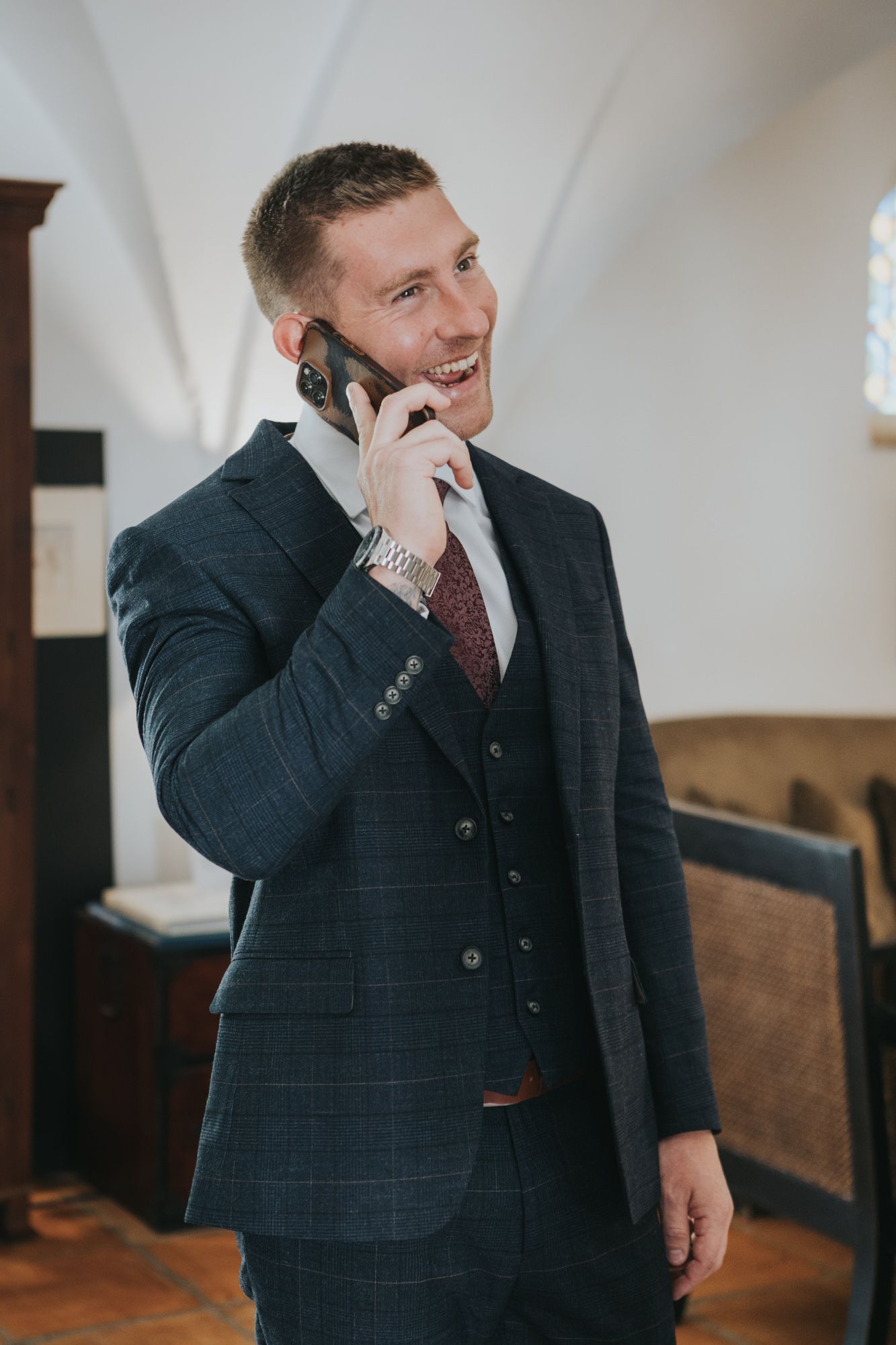Professional in a tailored navy suit making a phone call while smiling in a bright room.