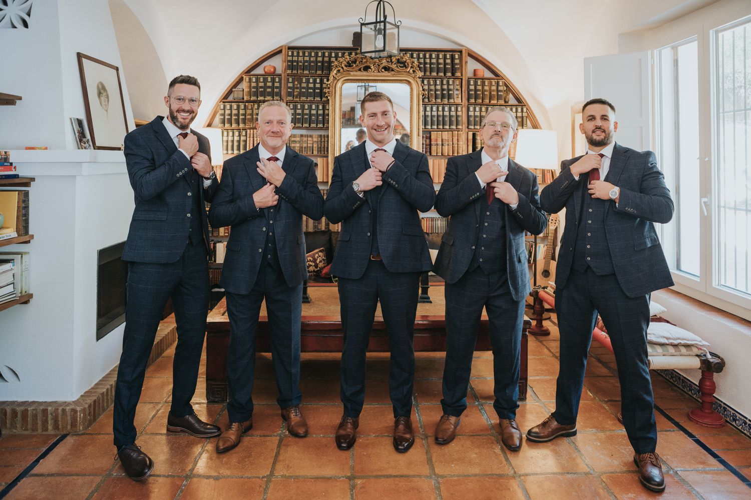Wedding party in black suits showing thumbs up gestures while standing in a formal interior setting.