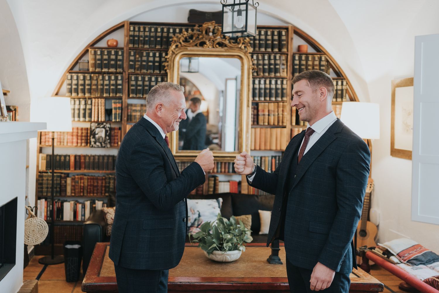 Two gentlemen in suits sharing a celebratory toast in a classic library setting.