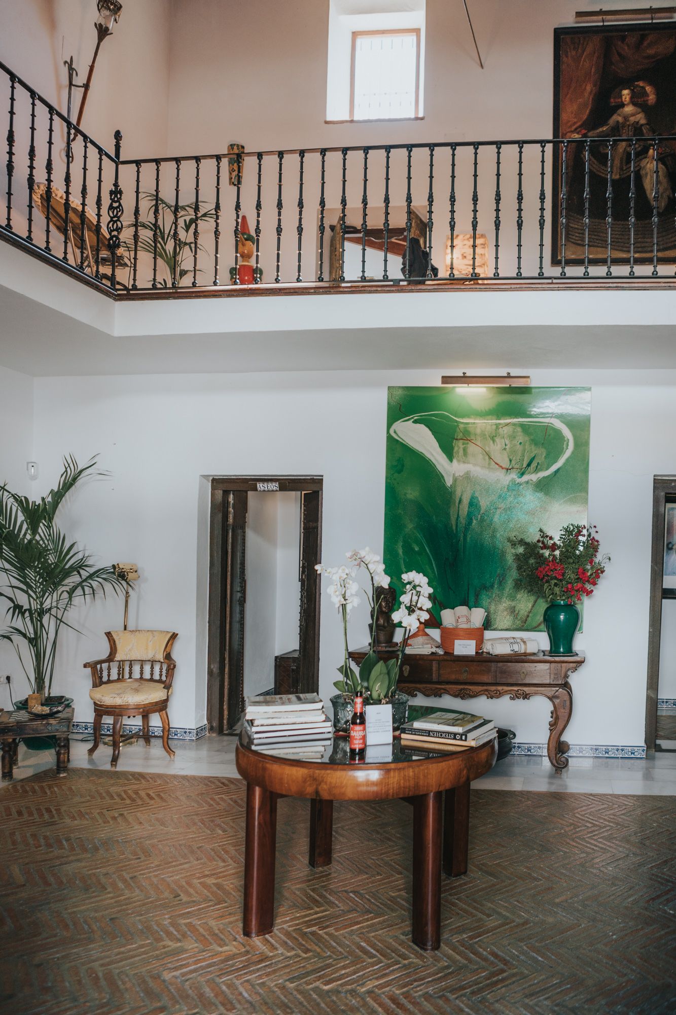 Elegant living room with herringbone floors, round coffee table, and balcony overlooking art-adorned walls.