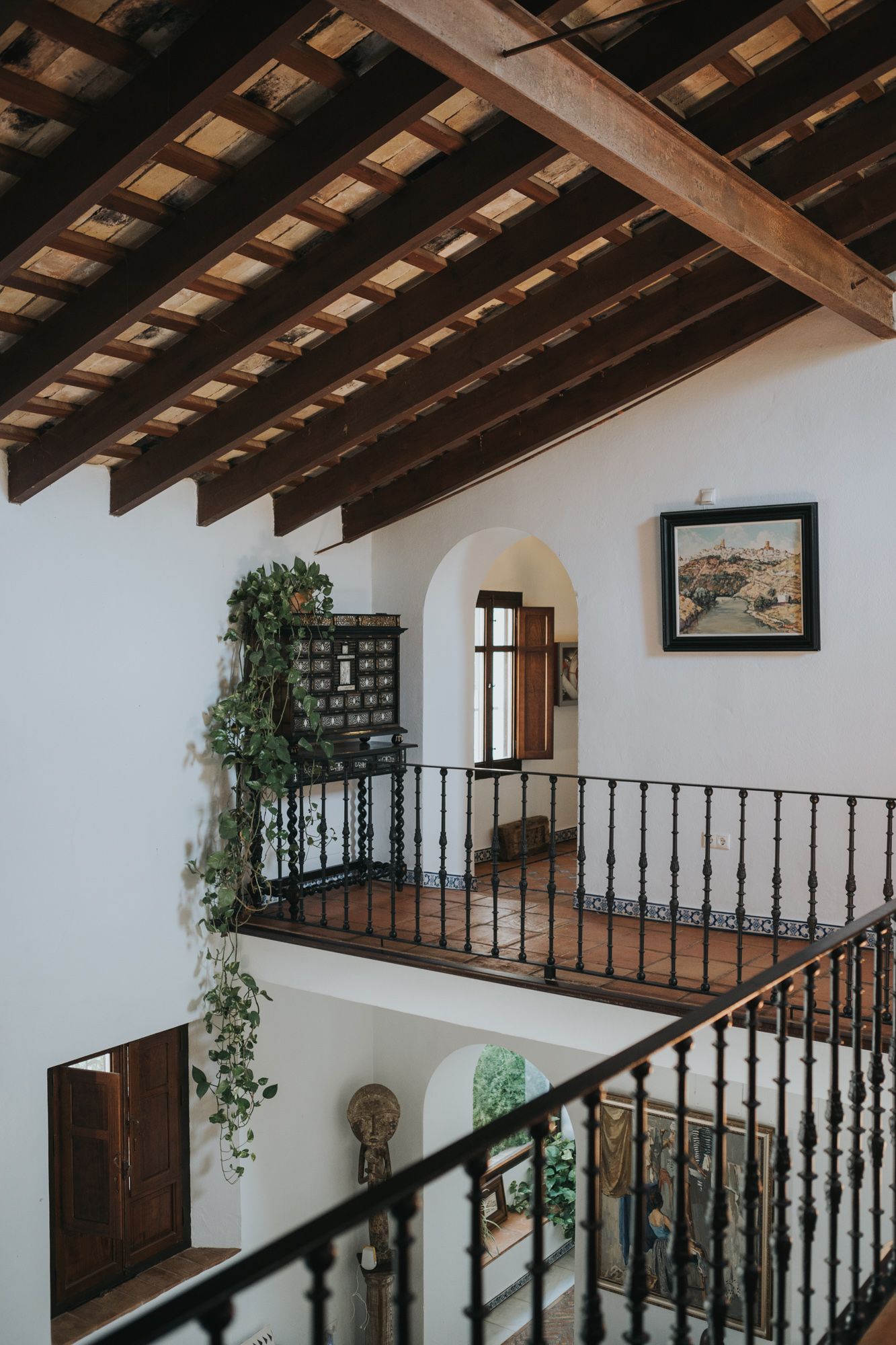 Spanish-style interior with exposed wooden beam ceiling, white walls and decorative iron railing.