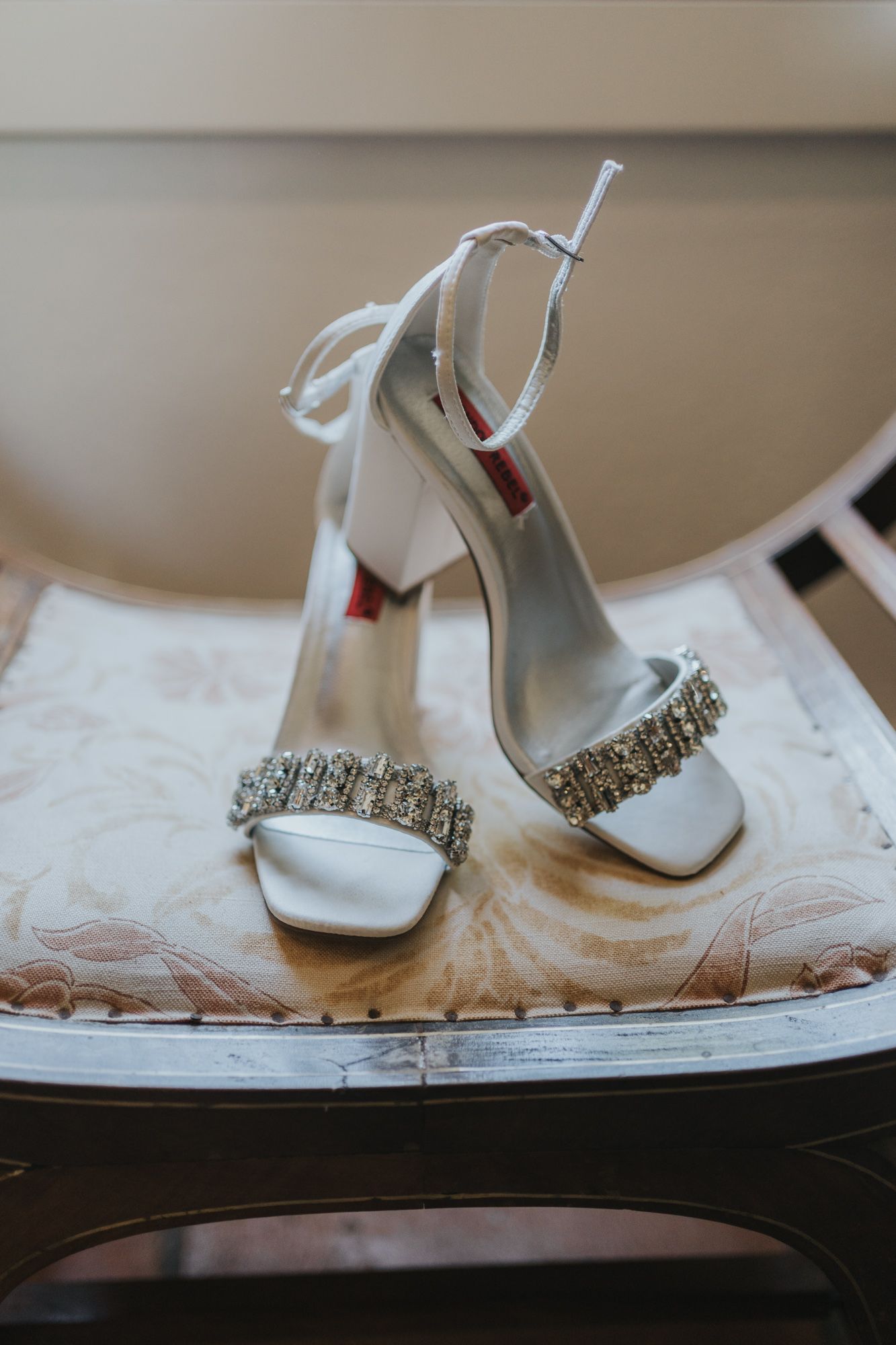 Elegant white wedding heels with crystal embellishments and ankle straps displayed on decorative fabric.