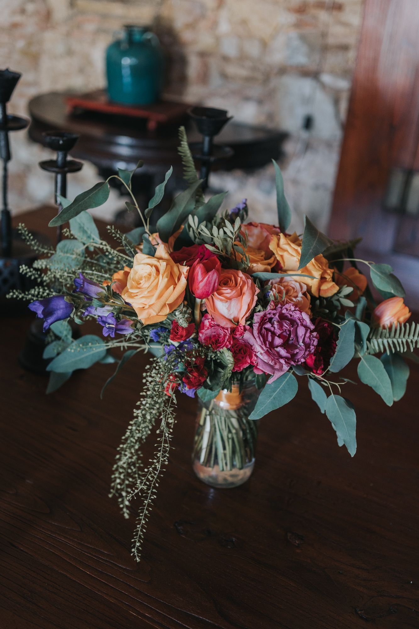 Vibrant floral arrangement with pink, orange and purple blooms mixed with eucalyptus in a clear vase.